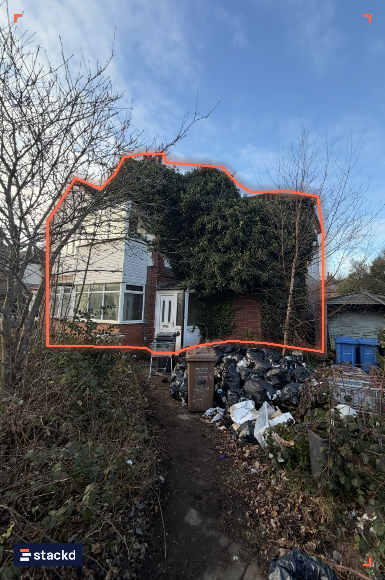 Semi-detached house overgrown with ivy, its front garden full of waste before refurbishment